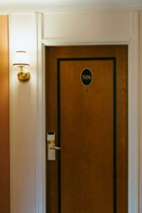 Close-up of a hotel room door with number 506 and a stylish wall-mounted brass lamp.