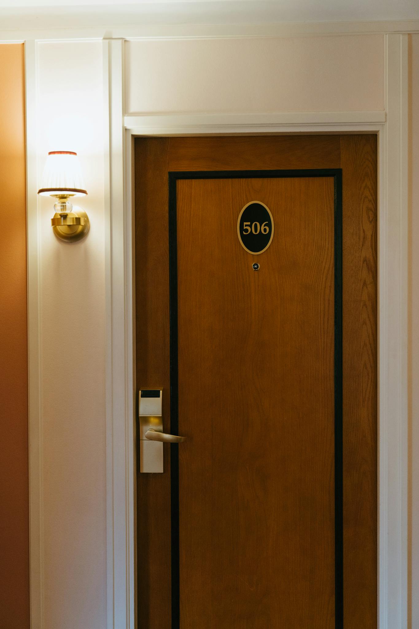 Close-up of a hotel room door with number 506 and a stylish wall-mounted brass lamp.