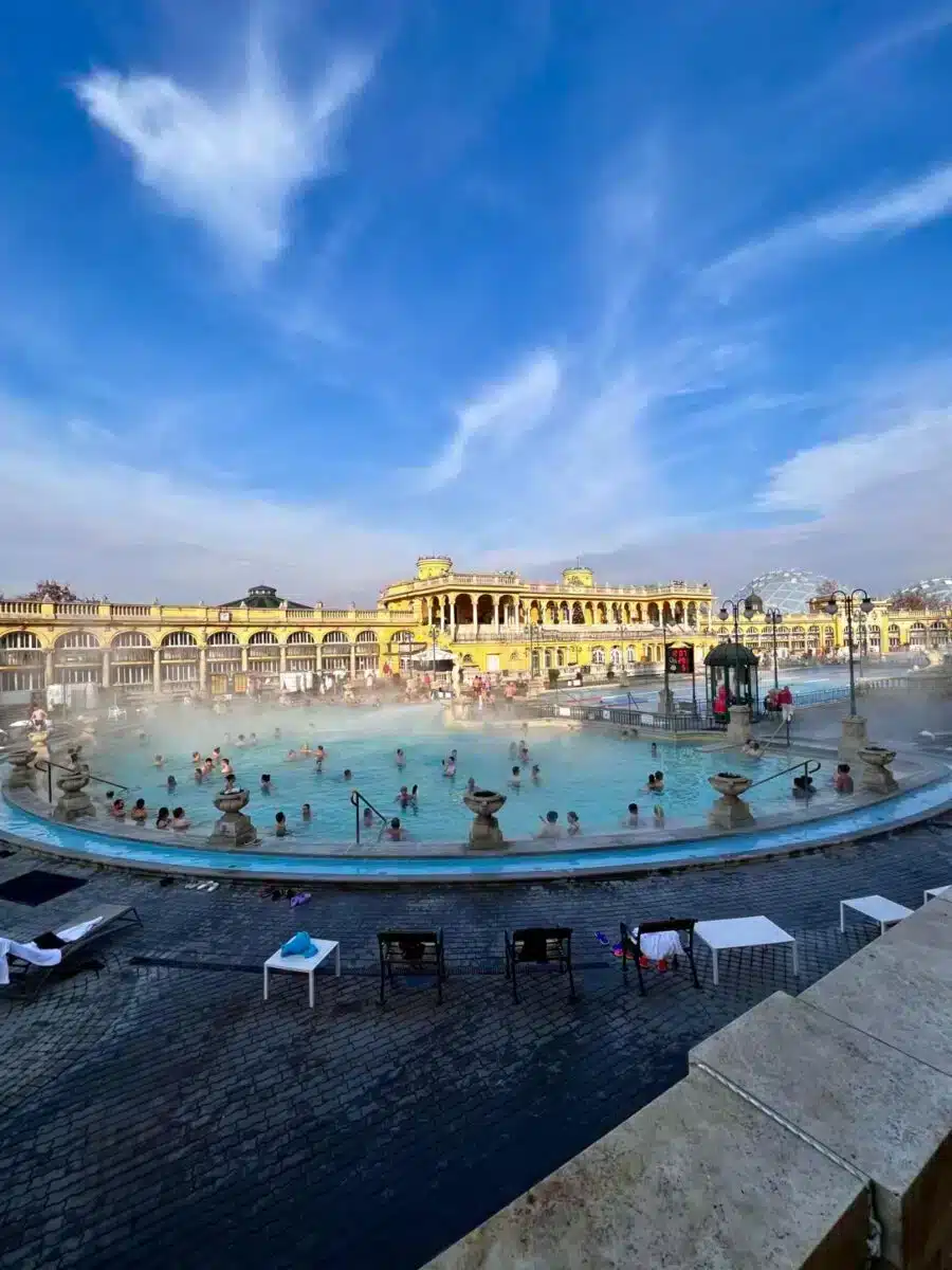 Panoramablick auf das belebte Außenbecken des Széchenyi Thermalbads Budapest mit gelber neobarocker Architektur