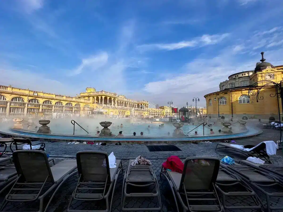 Dampfendes Außenbecken im Széchenyi Thermalbad Budapest mit neobarocker gelber Fassade und Liegestühlen im Winter