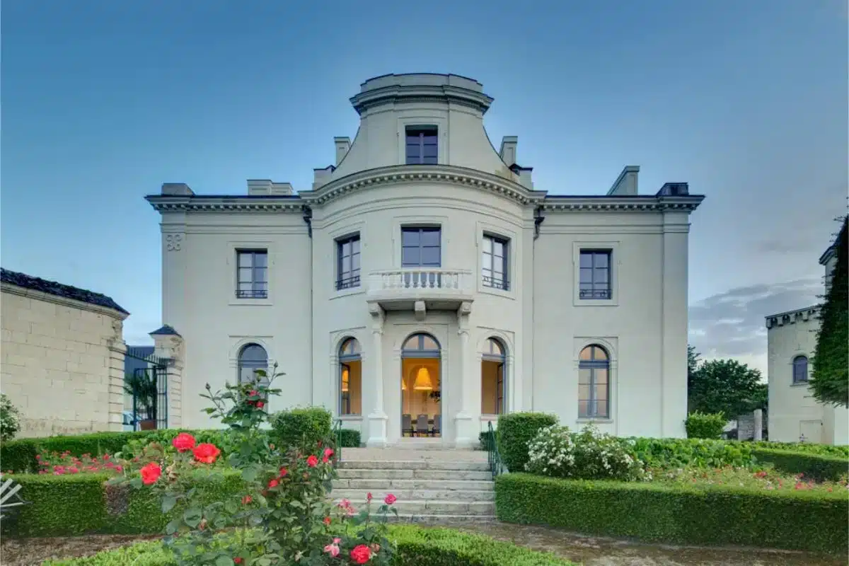 Neoklassizistische Fassade des Château de Candes im Loire-Tal mit beleuchtetem Eingang, Rosengarten und Bogenfenstern im Erdgeschoss in der Dämmerung