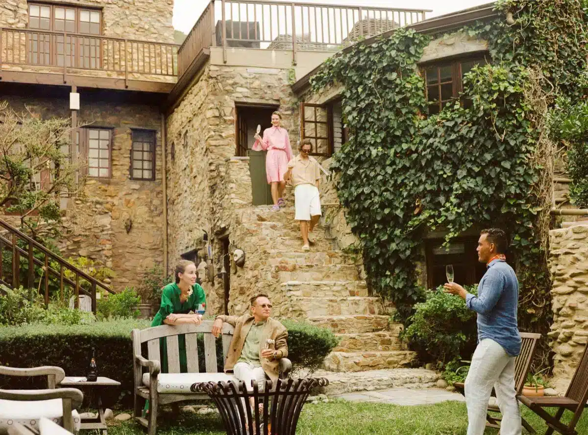 Gäste entspannen sich im Garten einer efeuumrankten Steinvilla, gebucht über Insider Villas, mit Personen auf Gartenbänken bei Getränken und Gesprächen