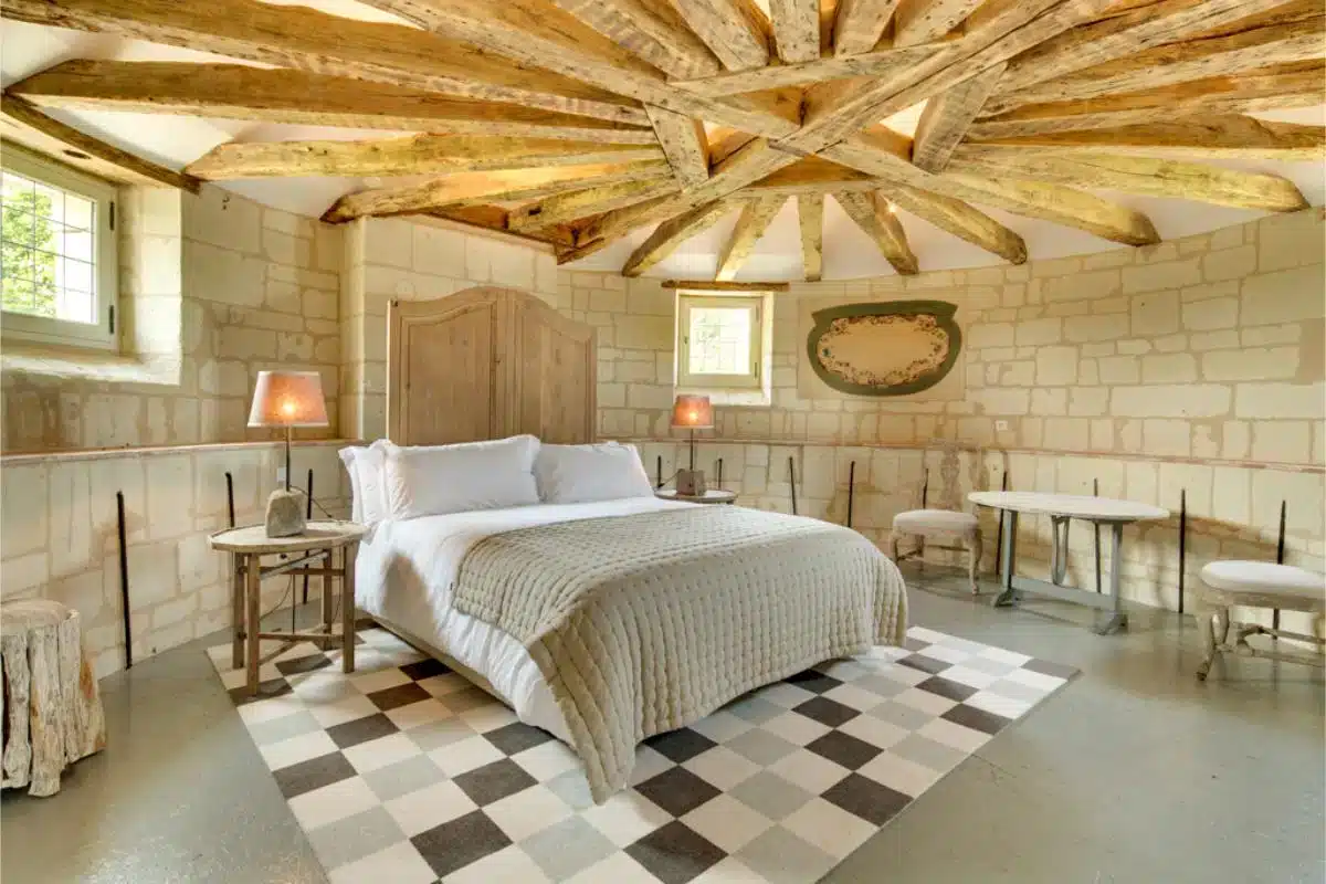 Turmschlafzimmer im Château de Candes im Loire-Tal mit freiliegender Holzbalkendecke, Steinwänden, weißem Leinenbett und schwarz-weißem Schachbrettfliesenboden