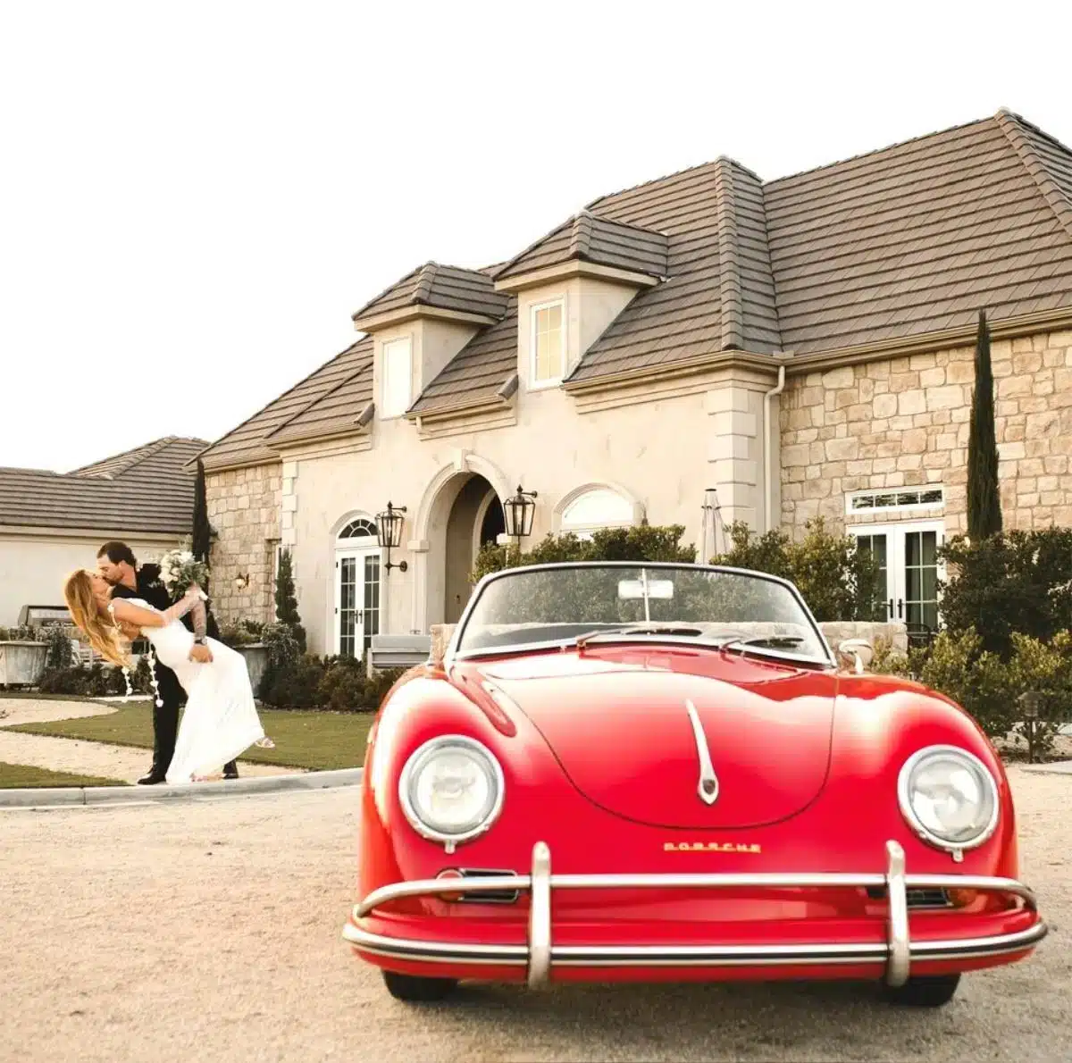 Brautpaar teilt einen romantischen Kuss vor einem klassischen roten Porsche 356 Cabrio vor dem Anwesen von Domaine Chardonnay