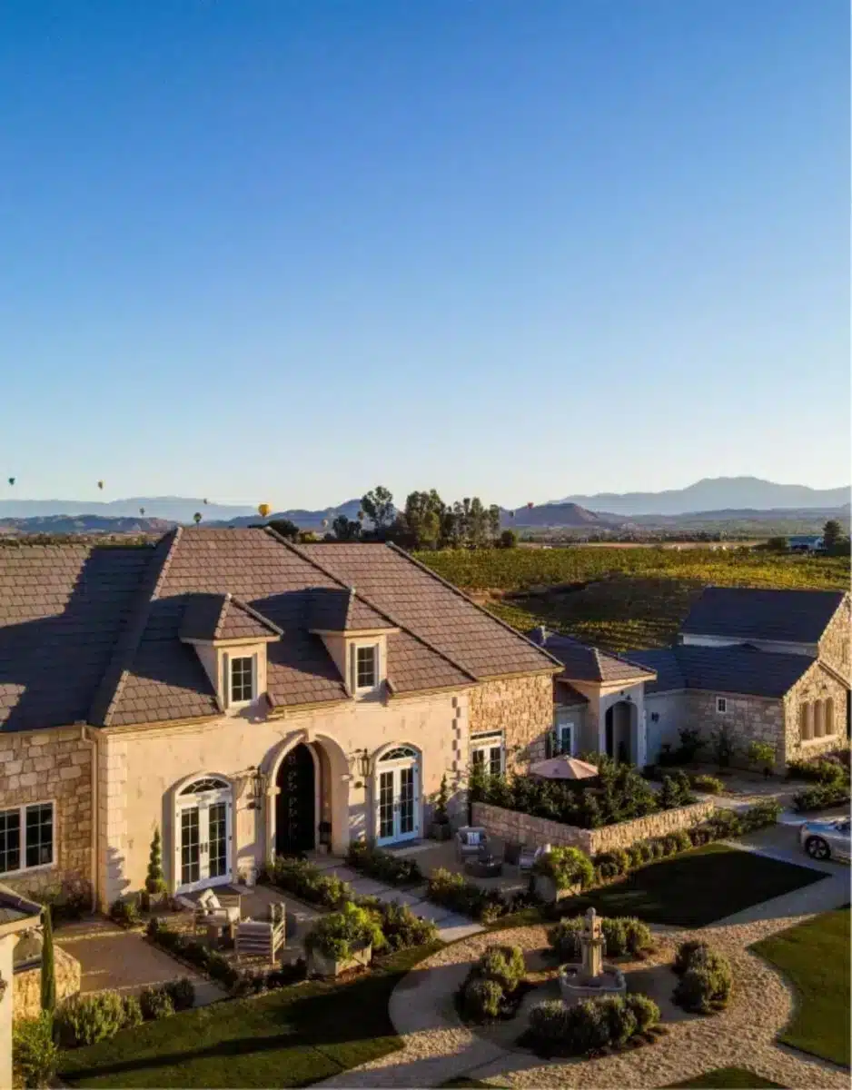 Luftaufnahme des Anwesens Domaine Chardonnay in Temeculas Weinregion mit dem französisch inspirierten Hauptgebäude, umgebenden Chardonnay-Weinbergen und Bergpanorama