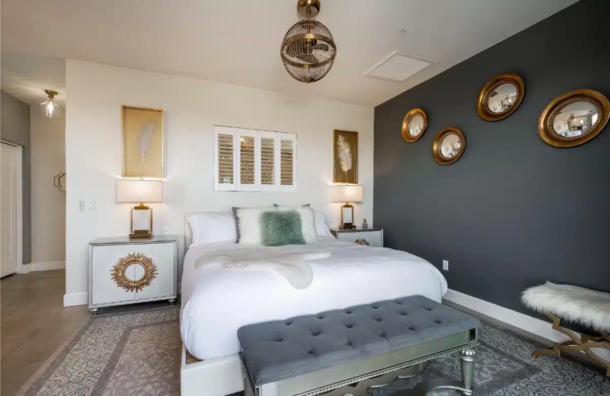 Elegant gestaltete Gästesuite in Domaine Chardonnay mit dunkelgrauer Akzentwand, Sonnenspiegel, Rattan-Pendelleuchte und frischer weißer Bettwäsche