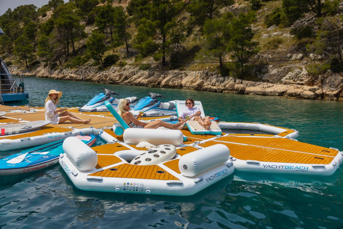 Gäste entspannen auf aufblasbaren Wasserspielzeugen neben einer Luxusyacht im türkisfarbenen kroatischen Gewässer