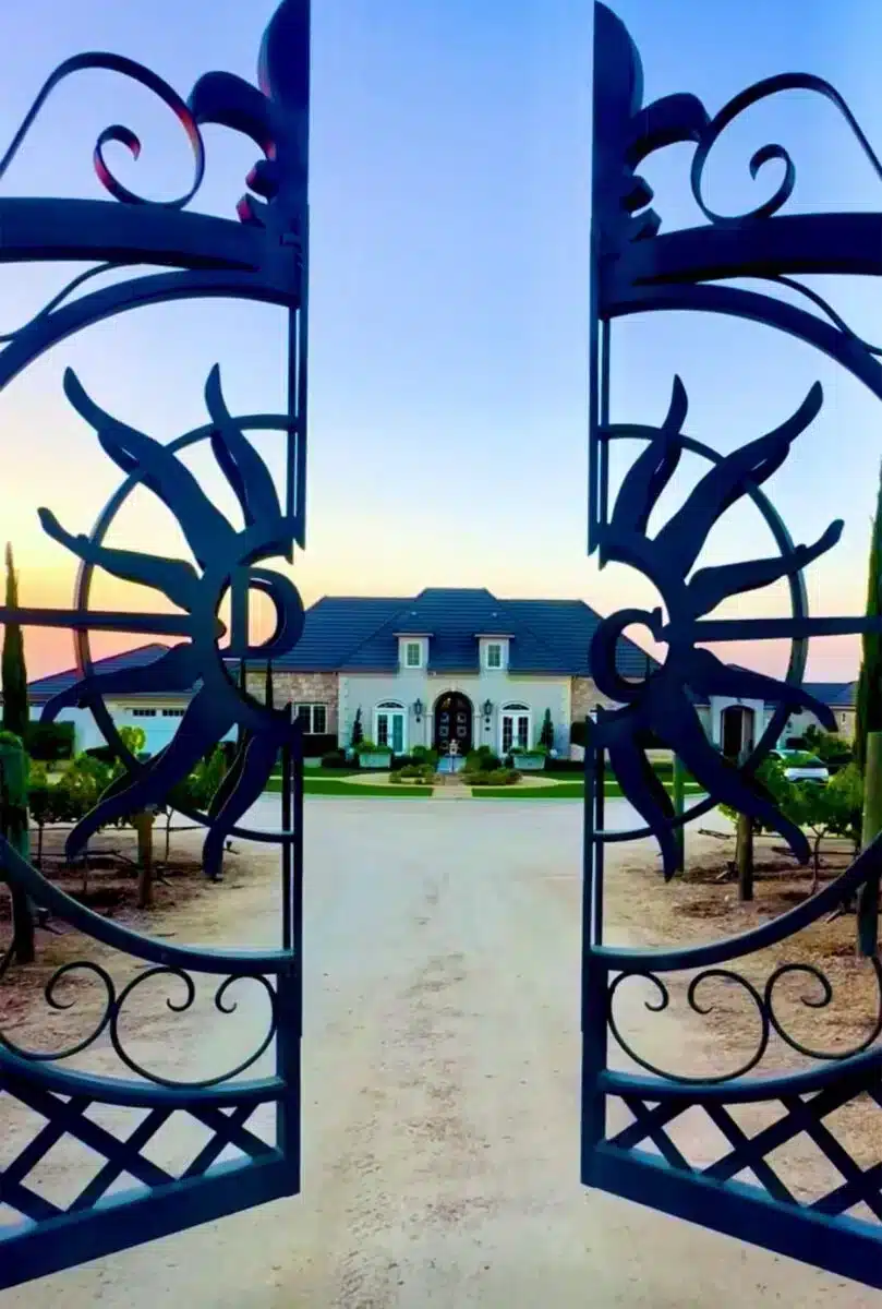 Kunstvolles schmiedeeisernes Eingangstor von Domaine Chardonnay mit Blick auf das Hauptgebäude und die gepflegte Gartenanlage in der Abenddämmerung