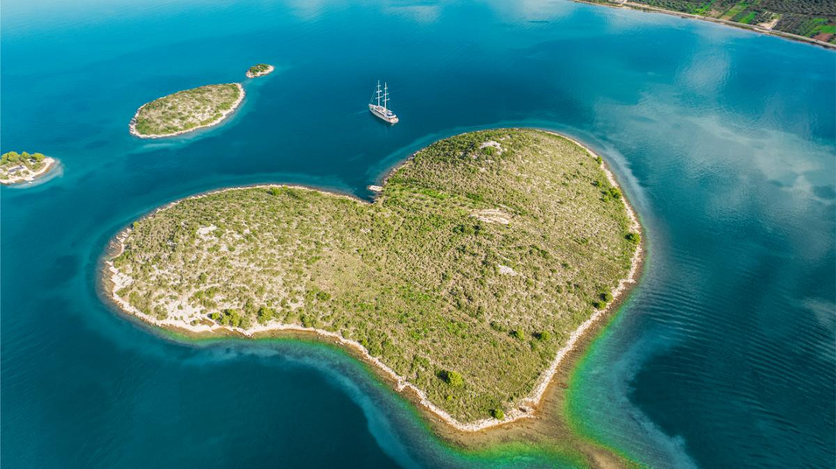 Drohnenaufnahme der Yacht Maxita beim Kreuzen nahe einer grünen kroatischen Insel mit türkisfarbenem Wasser