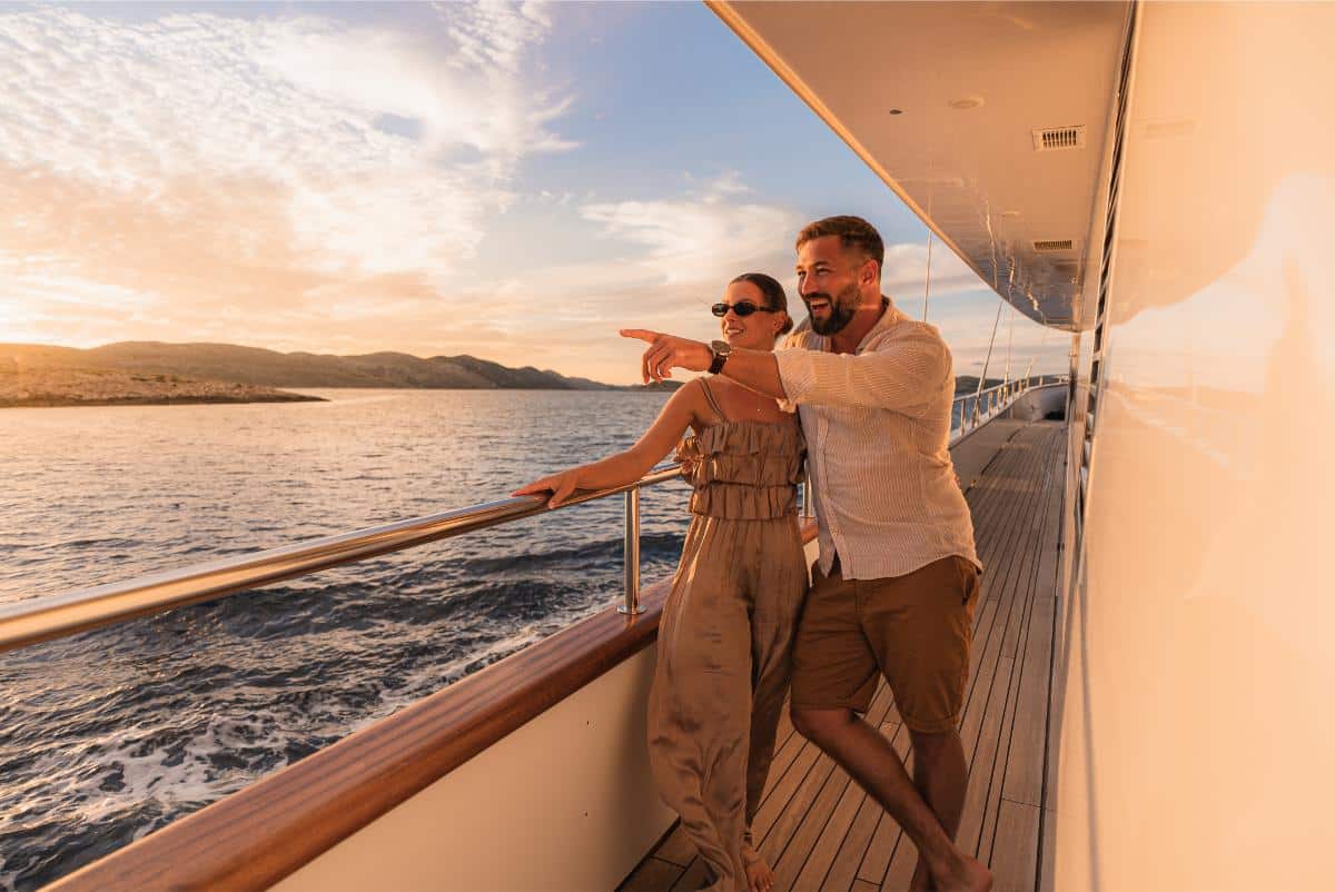 Paar posiert auf dem Yachtdeck bei Sonnenuntergang mit einer historischen kroatischen Küstenstadt im Hintergrund