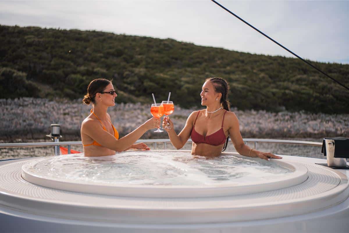 Paar stößt mit Cocktails im Whirlpool auf dem Sonnendeck einer Luxusyacht mit Meerblick an