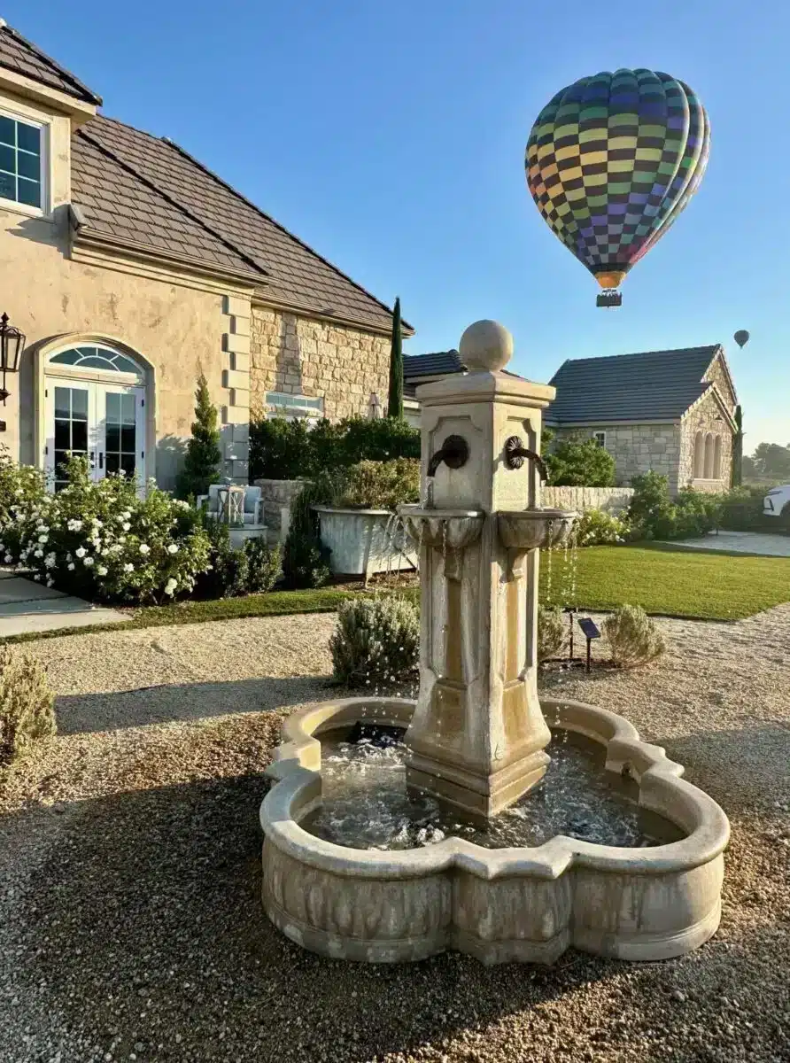 Steinerner Innenhofbrunnen auf dem Weingut Domaine Chardonnay in Temecula mit einem Heißluftballon über dem Anwesen am Morgenhimmel