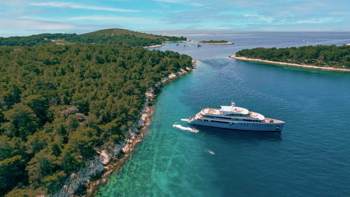 Luftaufnahme der Luxusyacht Ohana vor Anker nahe einer üppig grünen kroatischen Insel mit türkisfarbenem Wasser