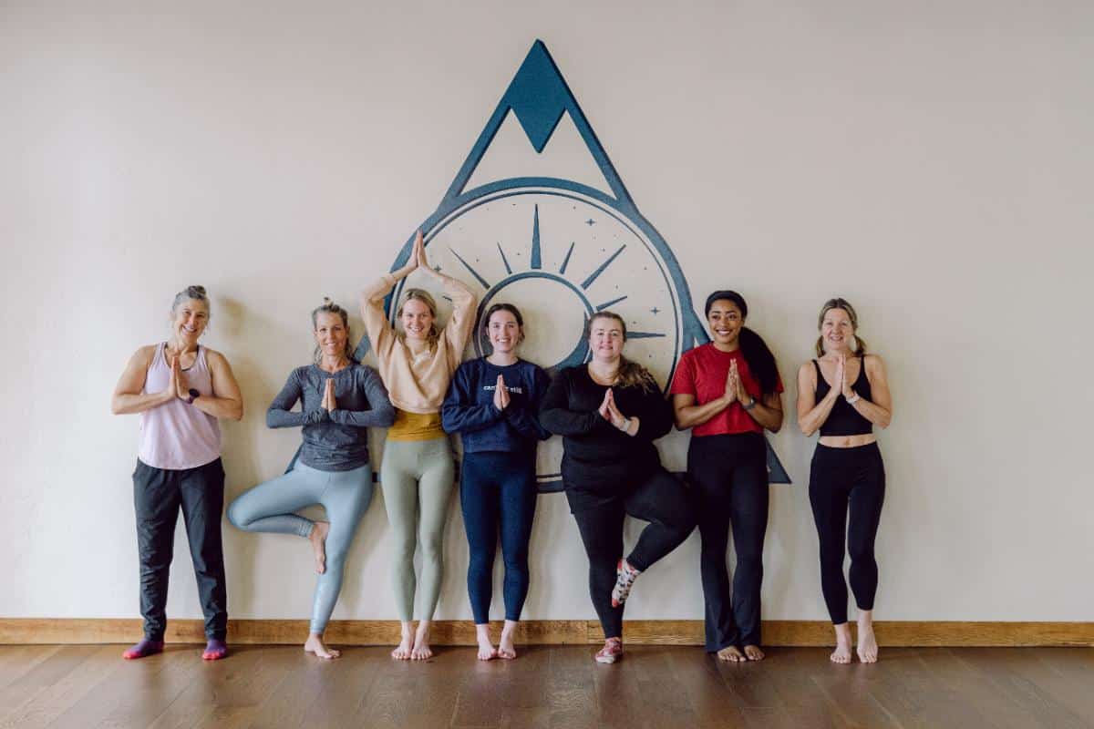 Group of women in tree pose during a yoga session at The Retreat Company studio with the mountain logo on the wall