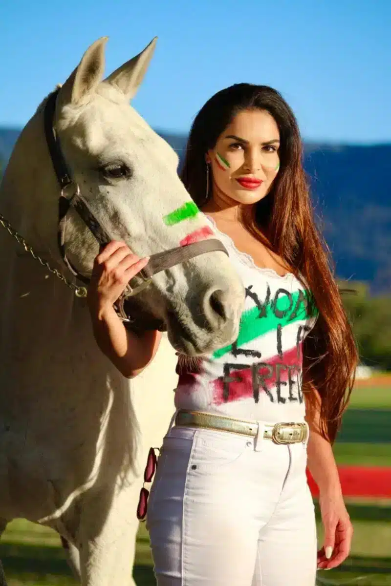 Sayé Yabandeh posiert mit einem weißen Pferd und trägt ein bemaltes T-Shirt