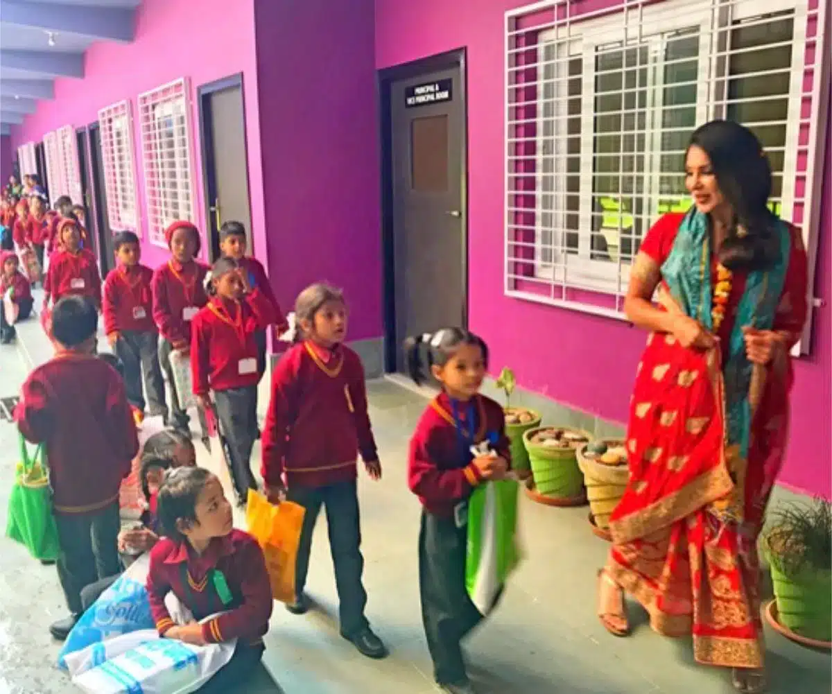 Sayé Yabandeh in einem traditionellen roten Sari mit Schulkindern in Uniformen vor einer Schule in Indien