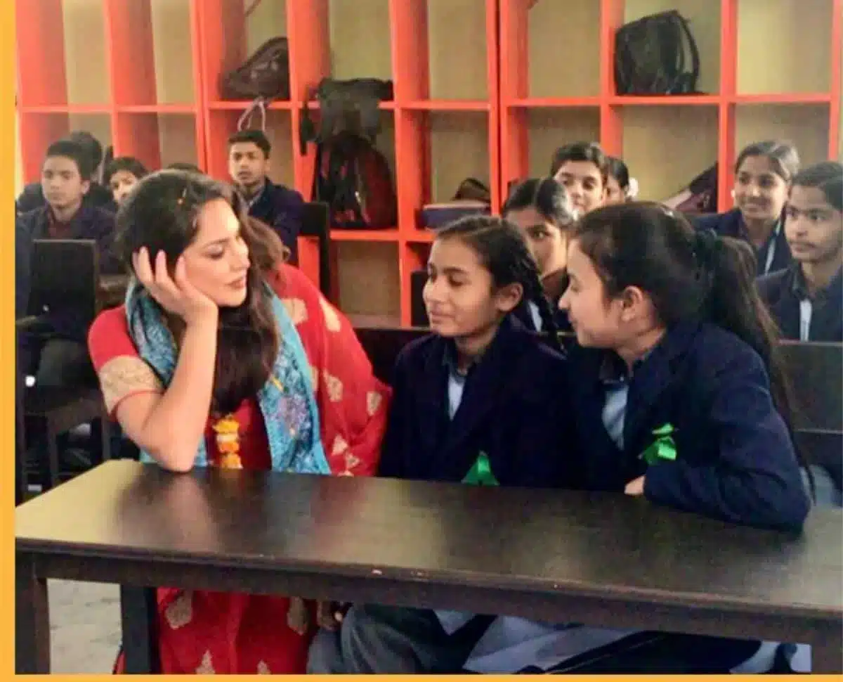 Sayé Yabandeh sitzt mit Schulkindern an einem Tisch in einem Klassenzimmer während eines Gemeinschaftsbesuchs von Sacred Ascension Journeys in Indien