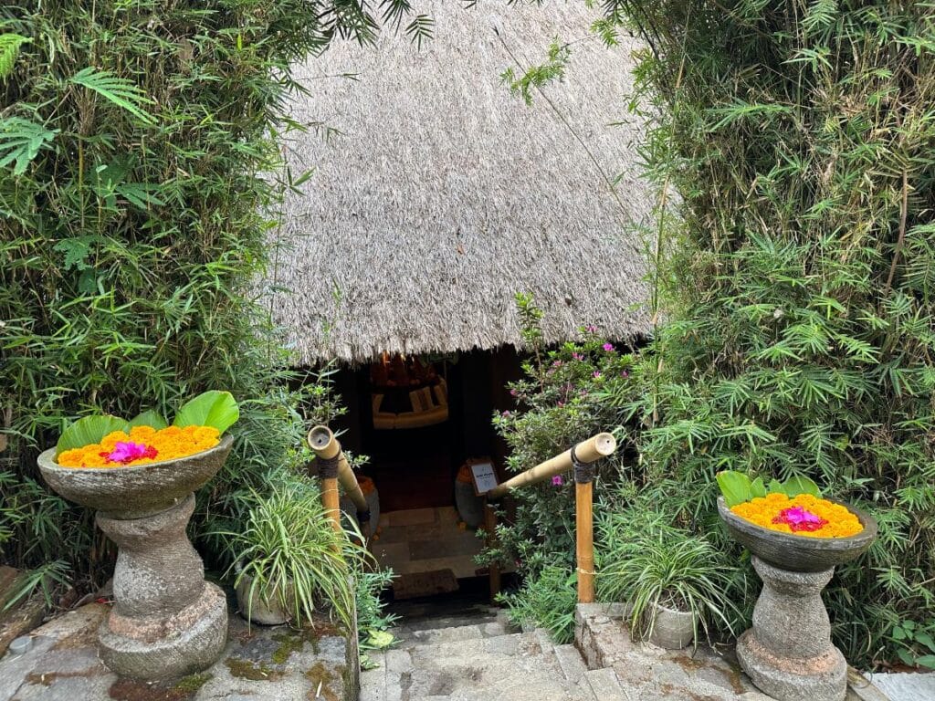 Traditioneller balinesischer Spa-Eingang der Munduk Moding Plantation mit geschnitzten Steinurnen, Ringelblumen-Opfergaben und Strohpavillon