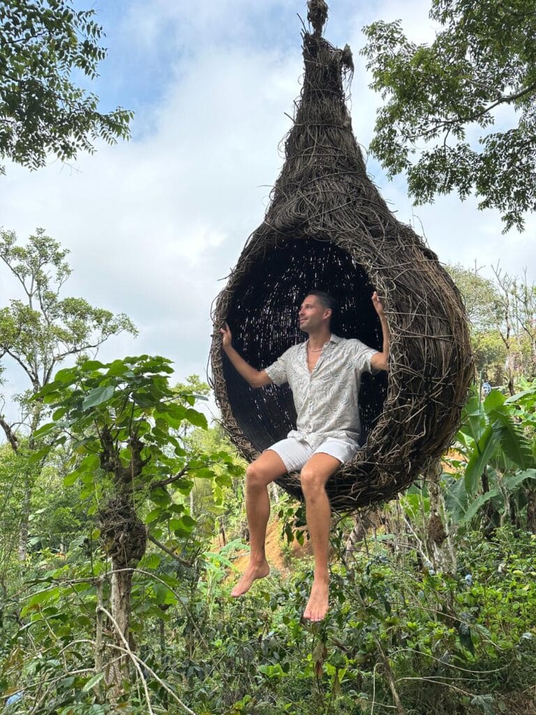 Gast sitzt in einer großen handgewebten Vogelnest-Kunstinstallation auf der Kaffeeplantage der Munduk Moding Plantation Bali