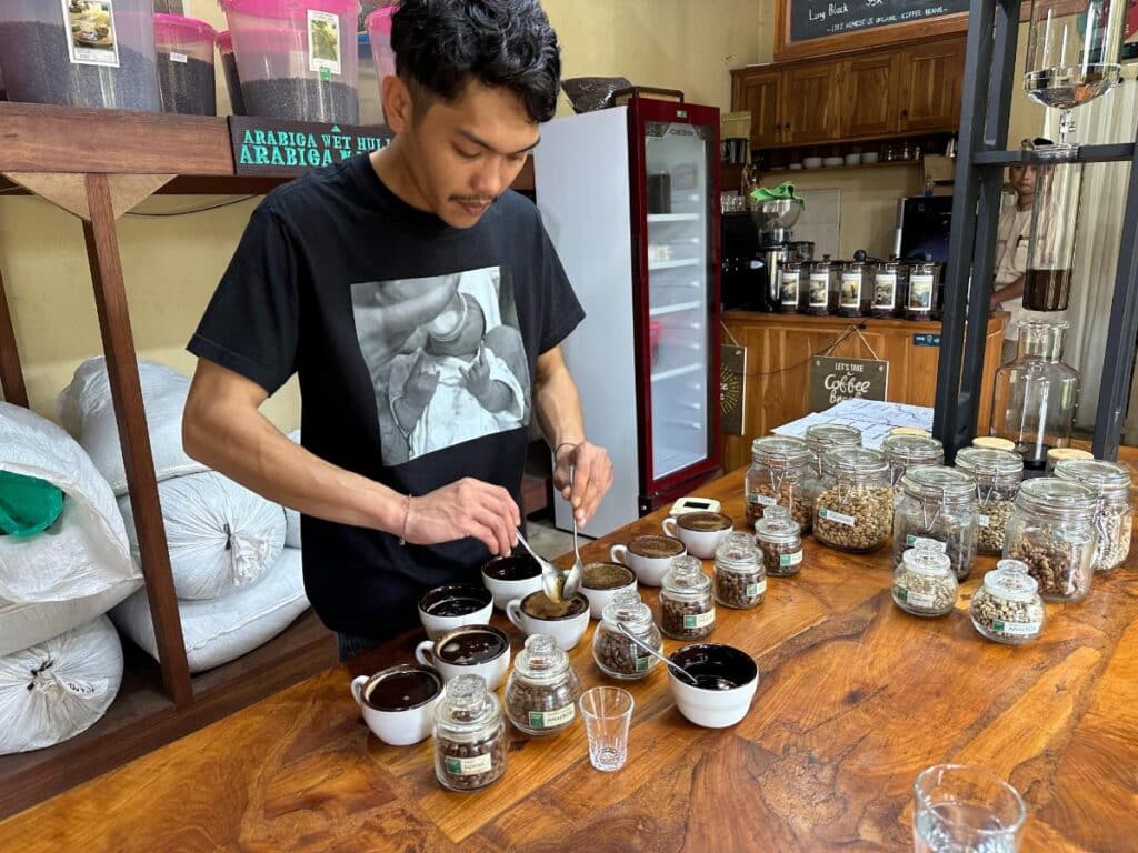 Barista bei einer Kaffeeverkostung in der Munduk Moding Plantation Bali, der frisch gebrühte Proben in Schalen gießt