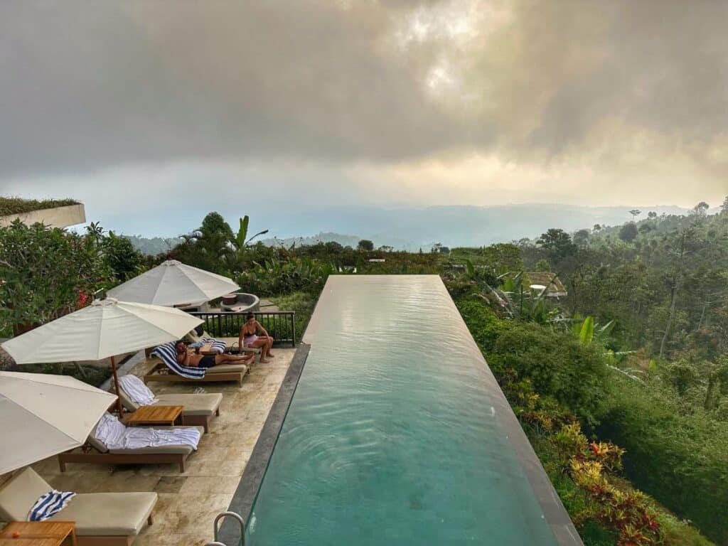Luftaufnahme des Haupt-Infinity-Pools der Munduk Moding Plantation Bali, der sich in der Abenddämmerung zum nebligen Hochlandtal erstreckt