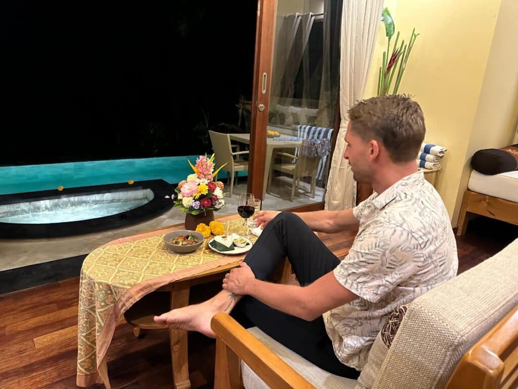 Gast sitzt am privaten Pool der Munduk Moding Plantation Bali am Abend und genießt Wein und Snacks am Wasser