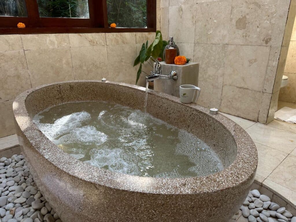 Gast genießt ein schwimmendes Frühstückstablett in der Vulkanstein-Badewanne der Munduk Moding Plantation Bali Villa