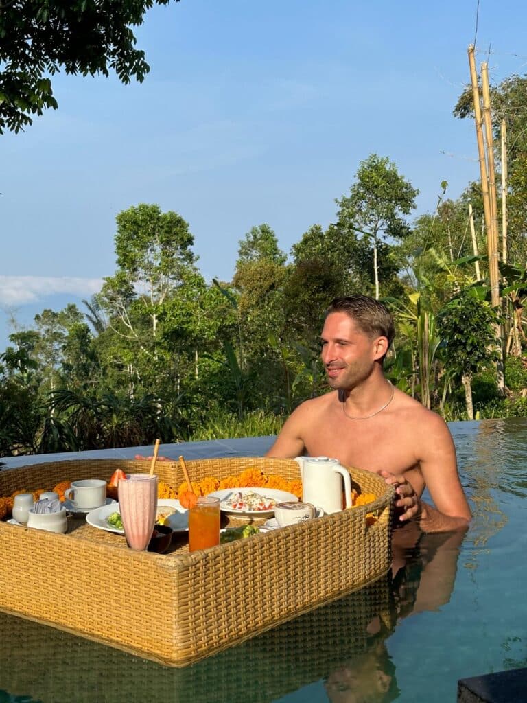 Mann genießt schwimmendes Frühstückstablett im privaten Infinity-Pool der Villa in der Munduk Moding Plantation Bali mit balinesischer Hochland-Dschungelkulisse