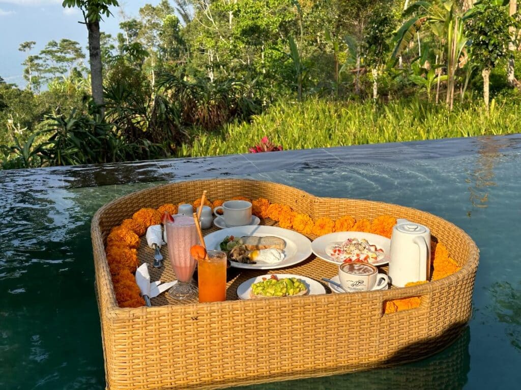 Herzförmiges schwimmendes Frühstückstablett aus Rattan im Villenpool der Munduk Moding Plantation Bali mit indonesischen Gerichten und tropischem Obst