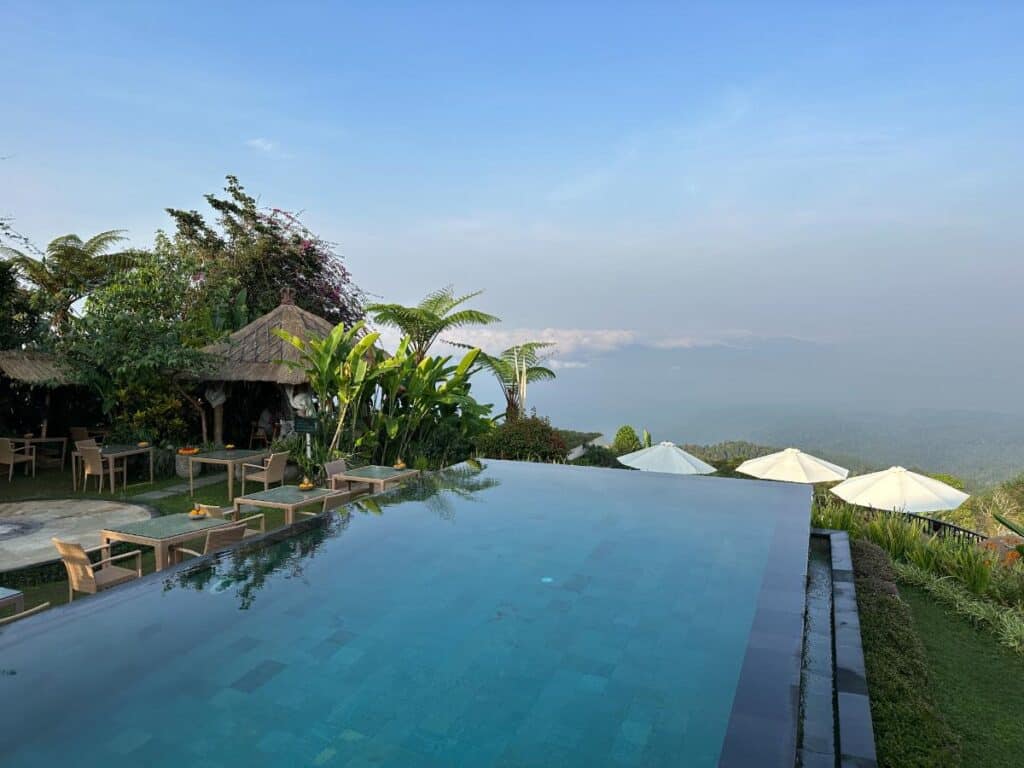 Infinity-Pool der Munduk Moding Plantation Bali mit strohgedecktem Bale-Pavillon, Palmen und gestufter Hochlandlandschaft