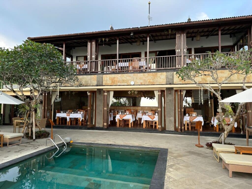 Hauptgebäude und Restaurantaußenbereich der Munduk Moding Plantation Bali am Pool mit Frangipanibäumen und Gästelounge-Bereich
