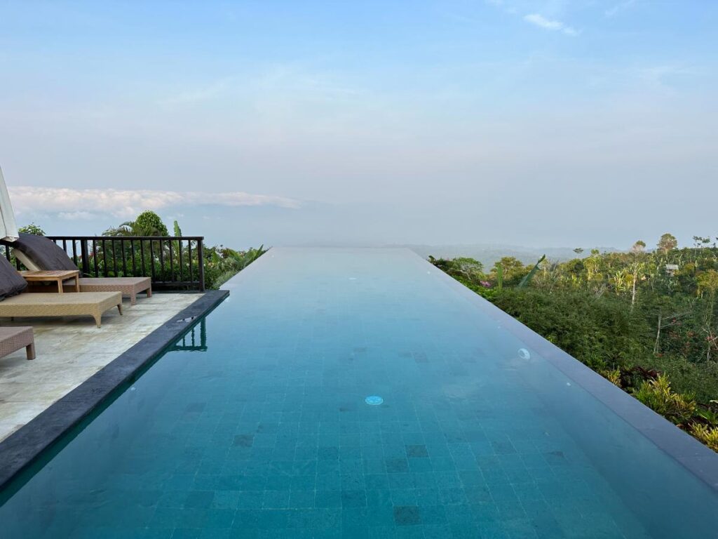 Morgenansicht des Haupt-Infinity-Pools der Munduk Moding Plantation Bali, der sich bei Sonnenaufgang in den klaren Hochlandhimmel erstreckt