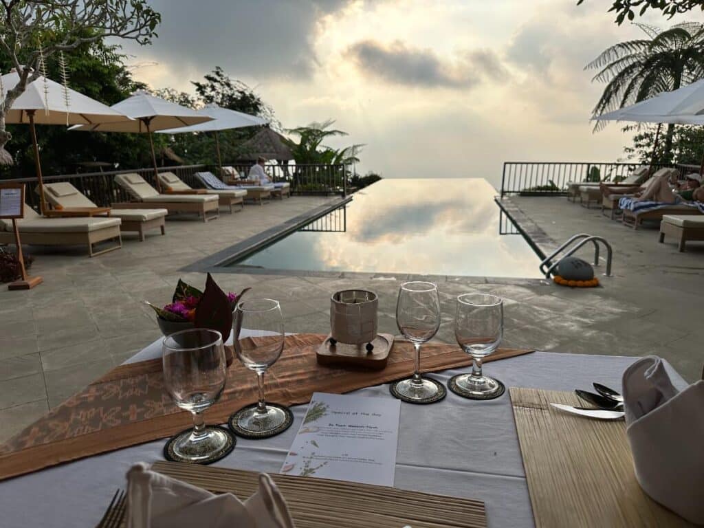 Gedeckter Esstisch am Pool mit Weingläsern in der Munduk Moding Plantation Bali mit Blick auf den Infinity-Pool bei Sonnenuntergang