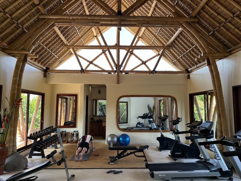 Fitnessraum und Trainingseinrichtungen der Munduk Moding Plantation Bali mit Gewichten, Spiegeln und offenen Fenstern mit Dschungelblick