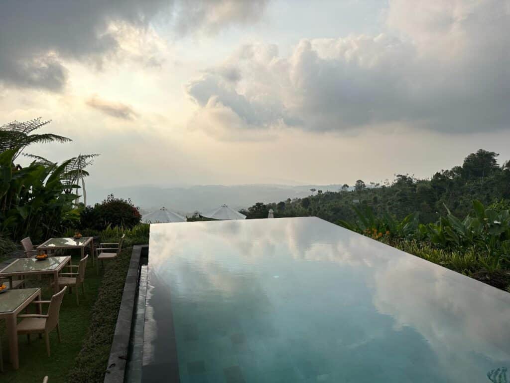 Blick auf Wasserebene des Infinity-Pools der Munduk Moding Plantation Bali mit sonnigem Himmel und fernem Hochlandplateau
