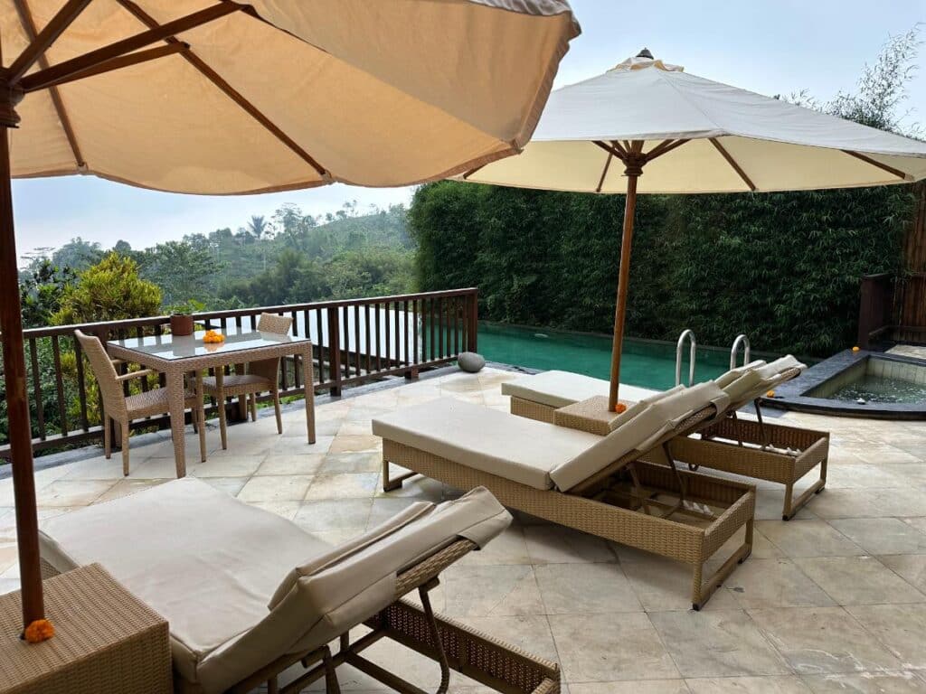 Resortterrasse mit Sonnenliegen, Sonnenschirmen und grünem Pool der Munduk Moding Plantation Bali inmitten tropischer Natur