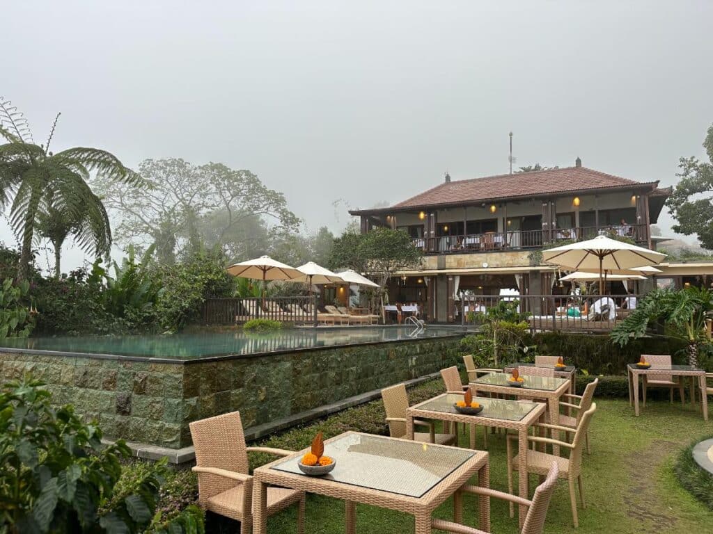 Hauptgebäude und Pool der Munduk Moding Plantation Bali in Morgennebel gehüllt mit tropischen Bäumen im Vordergrund