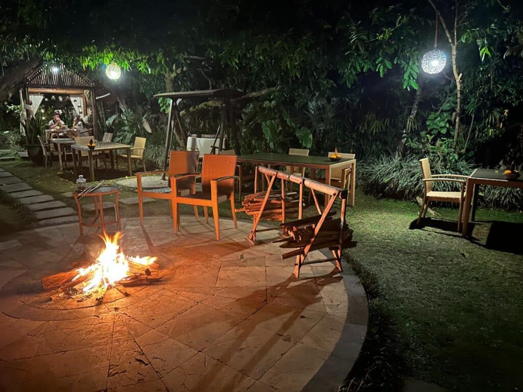 Abendlicher Lagerfeuer-Sitzbereich im Freien der Munduk Moding Plantation Bali mit Holzstühlen um eine Feuerstelle im Garten
