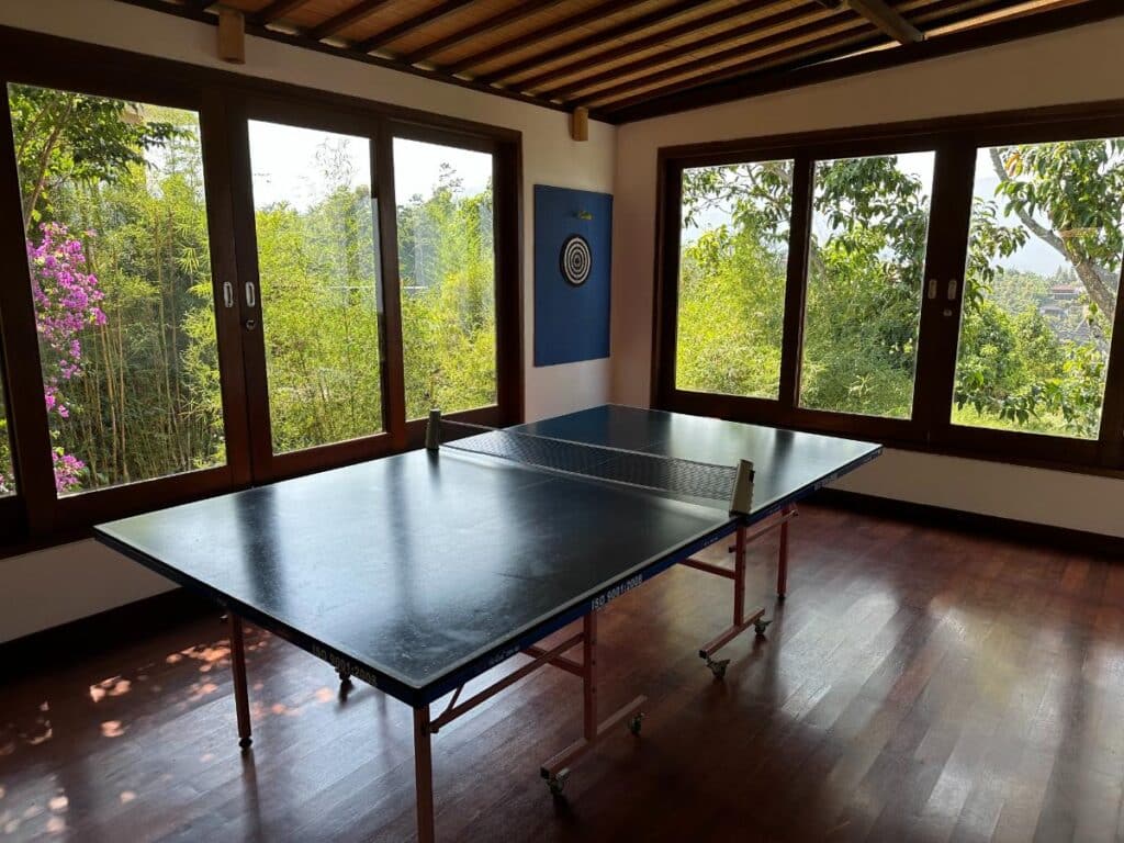 Freizeitraum der Munduk Moding Plantation Bali mit Tischtennisplatte und Panorama-Dschungelblick durch raumhohe Fenster