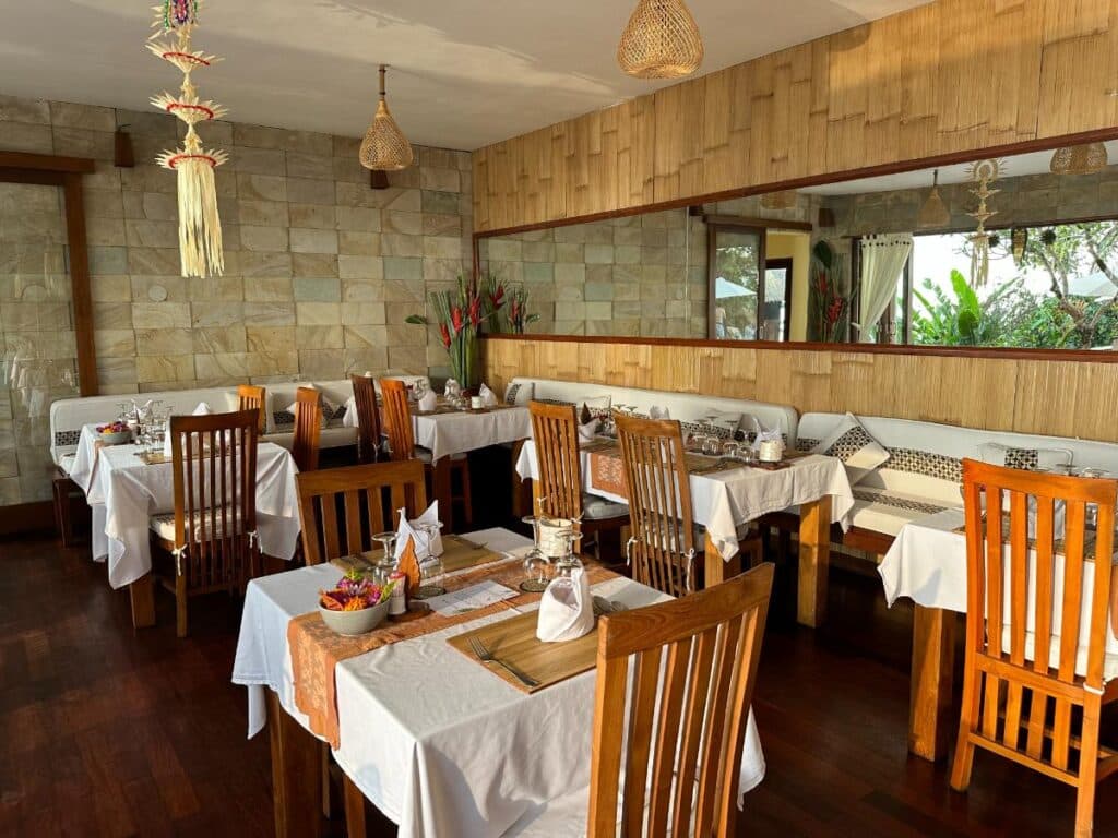Restaurantinnenraum der Munduk Moding Plantation Bali mit Bankettsitzplätzen, weißen Tischdecken und Holzstühlen