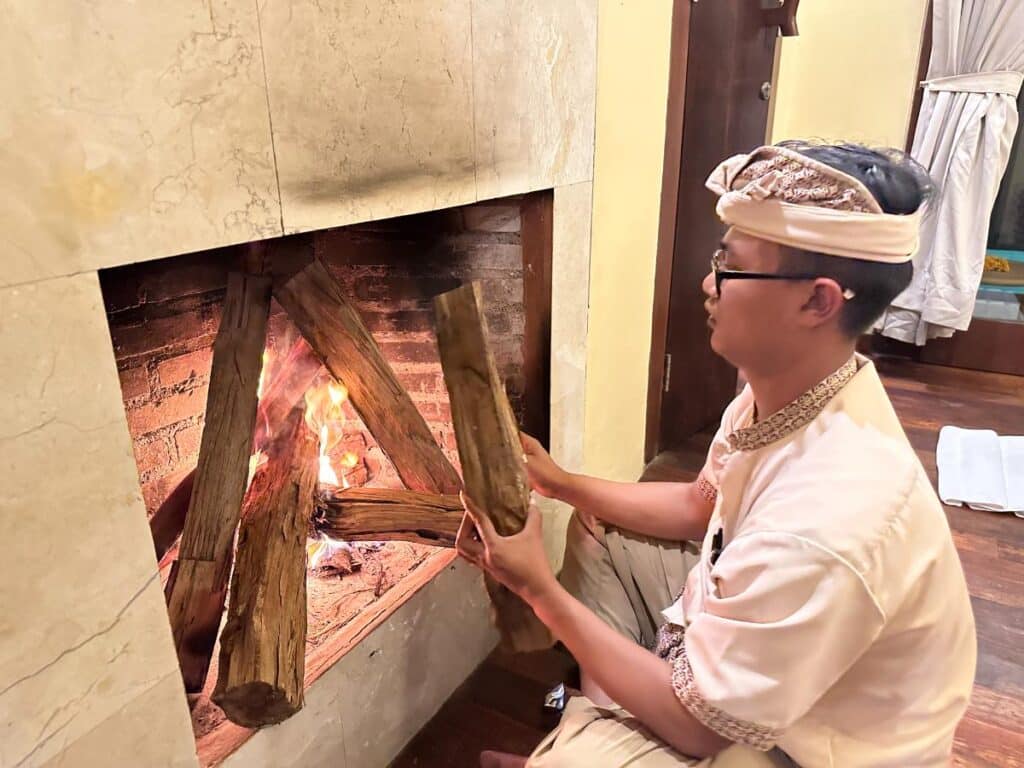 Balinesisches Teammitglied in traditioneller Kleidung entzündet sorgfältig den Kamin in der Villa der Munduk Moding Plantation Bali