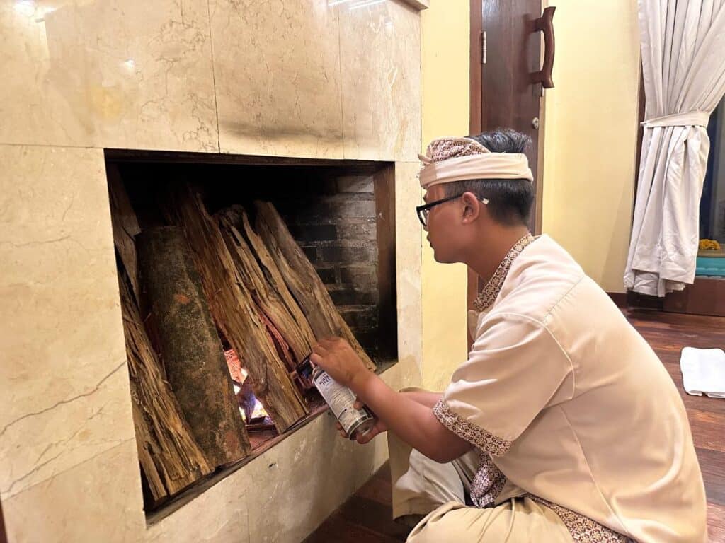 Balinesisches Teammitglied mit traditionellem balinesischem Udeng-Kopfschmuck stapelt Holzscheite zum Anzünden des Villenkamins in der Munduk Moding Plantation