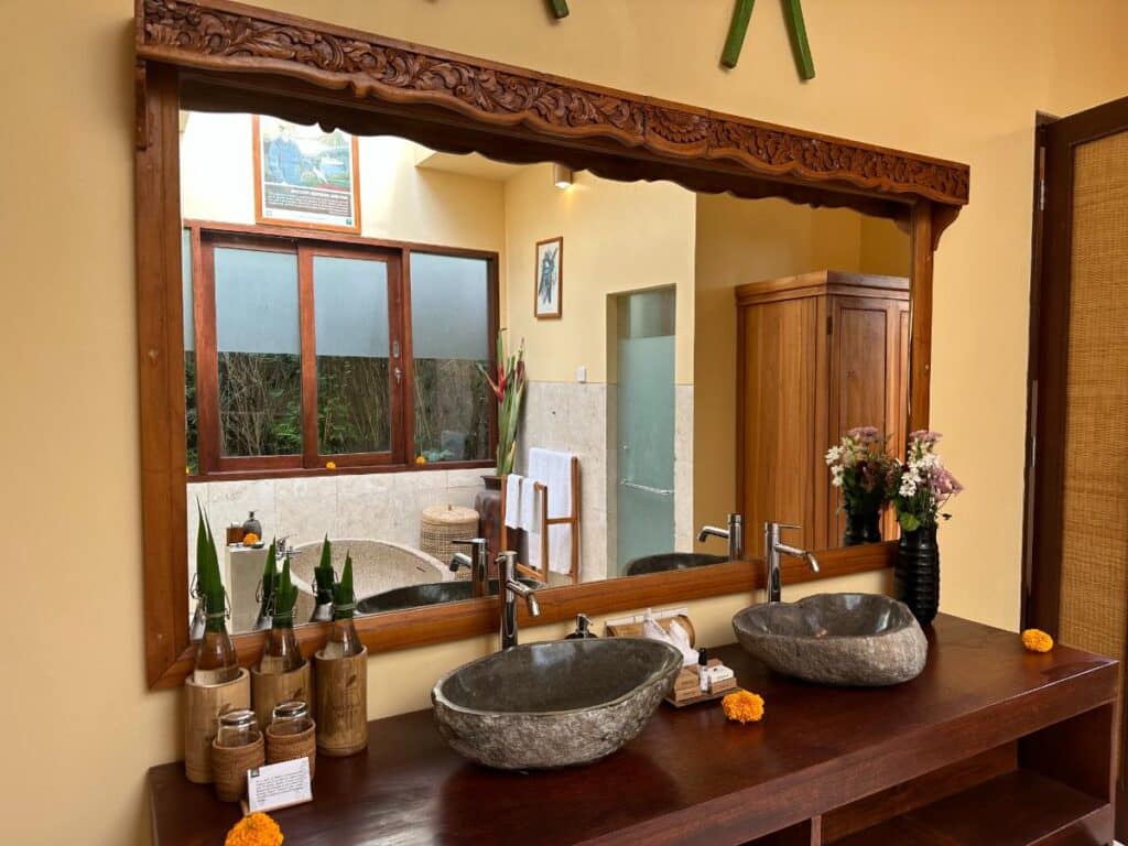 Doppelte handgeschnitzte Steinwaschbecken mit verziertem Holzspiegel-Rahmen im Badezimmer der Munduk Moding Plantation Bali Villa