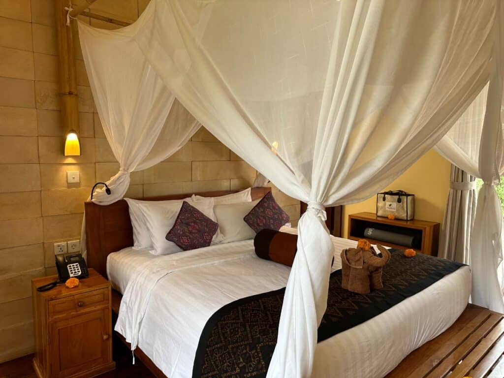 Frontansicht des Kingsize-Himmelbetts mit weißer Bettwäsche und lila Kissen im Schlafzimmer der Munduk Moding Plantation Bali Villa