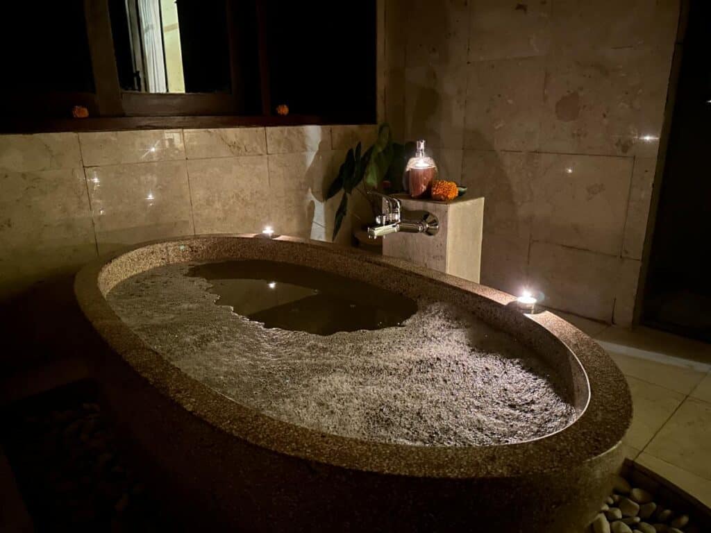 Geschnitzte Vulkanstein-Badewanne mit warmem Abendlicht im Badezimmer der Munduk Moding Plantation Bali Villa