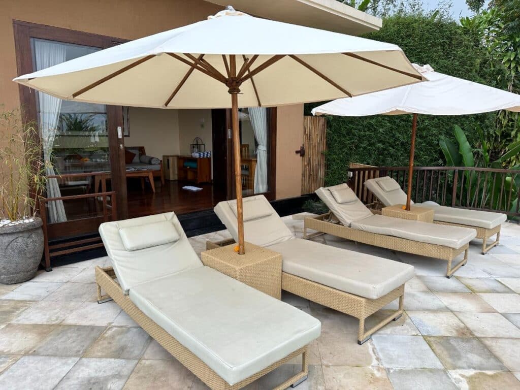 Außenterrasse der Villa in der Munduk Moding Plantation Bali mit Sonnenliegen, weißem Sonnenschirm und tropischer Dschungelumgebung