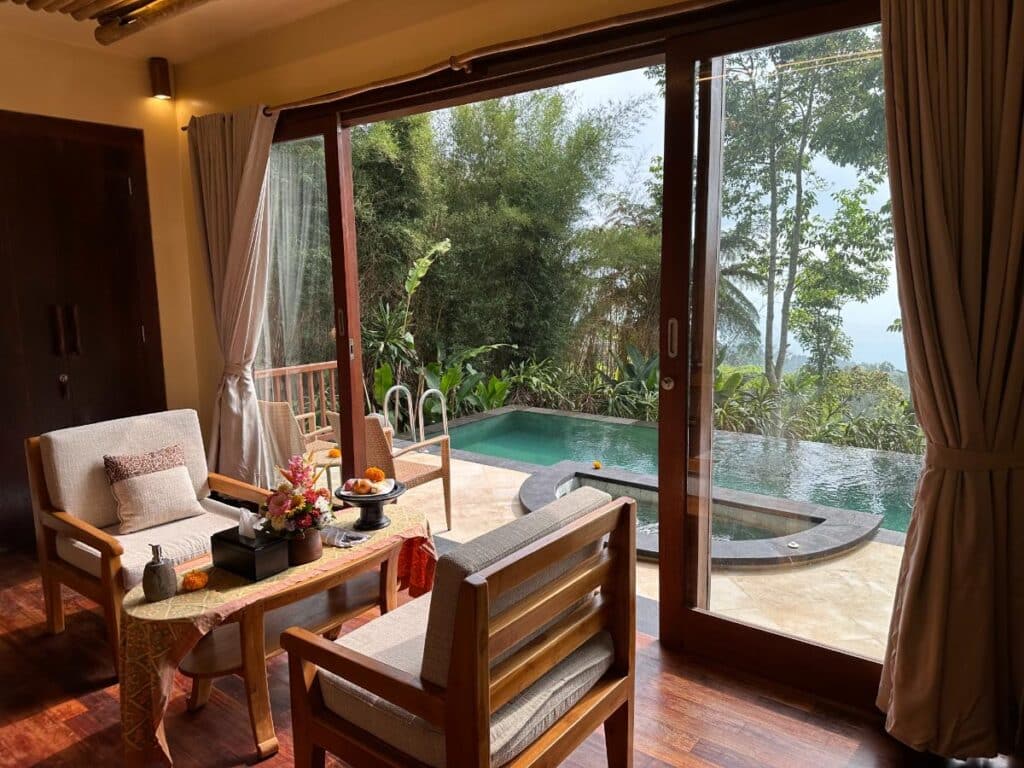 Offener Wohnbereich der Villa in der Munduk Moding Plantation Bali mit Glasschiebetüren zum privaten Pool und nebligem Hochlandblick