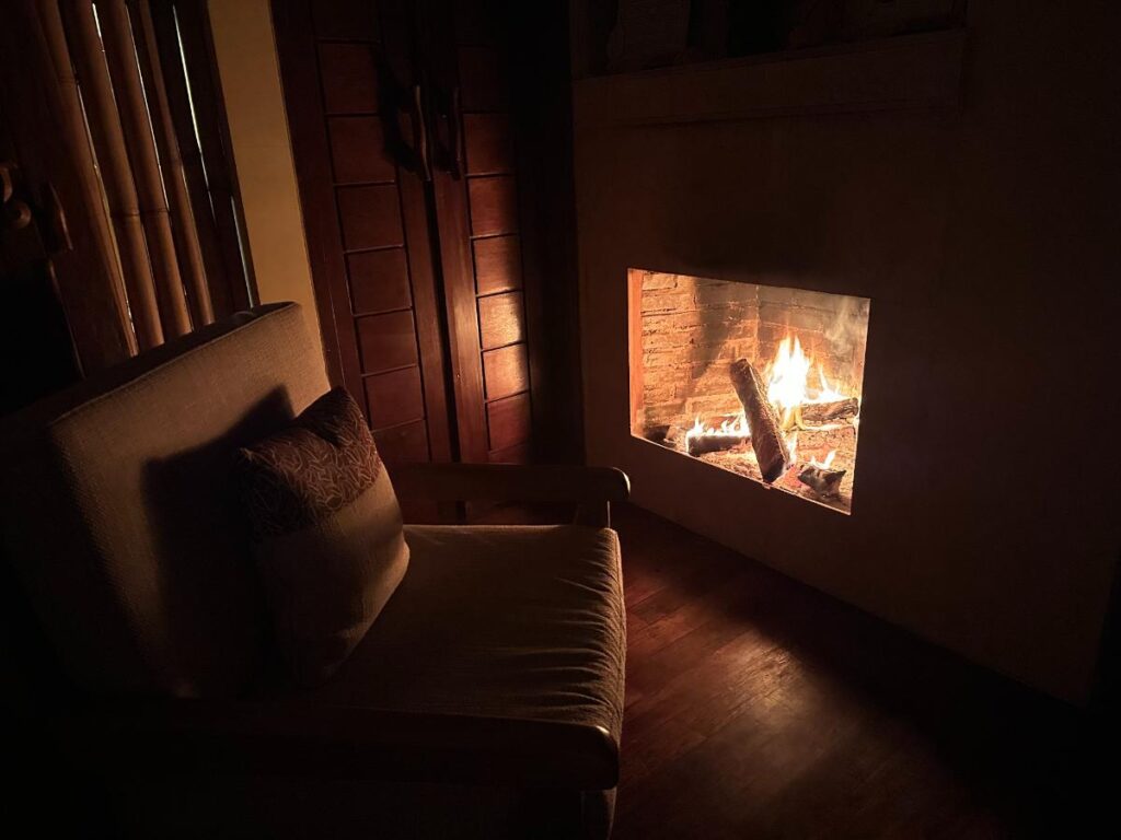 Gemütliches Villa-Interieur der Munduk Moding Plantation Bali bei Nacht mit warm glühendem Kamin im abgedunkelten Wohnzimmer