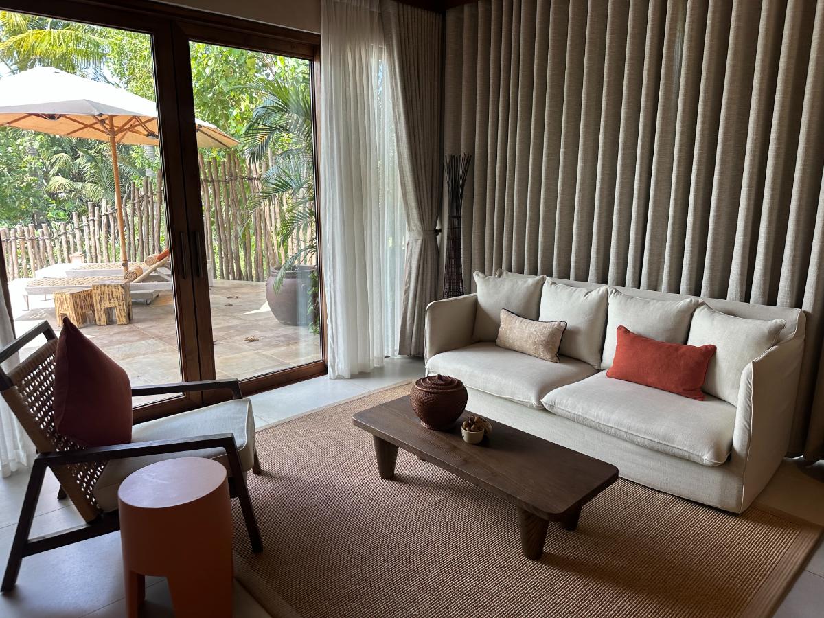 Pool villa lounge with sofa, low table and sliding doors to the pool, Namia River Retreat, Hoi An, Vietnam