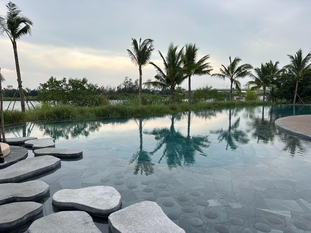 Infinity pool with stone stepping islands and palm reflections at dusk, Namia River Retreat, Hoi An, Vietnam